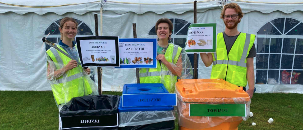 three smiling student staff with waste bins at an event